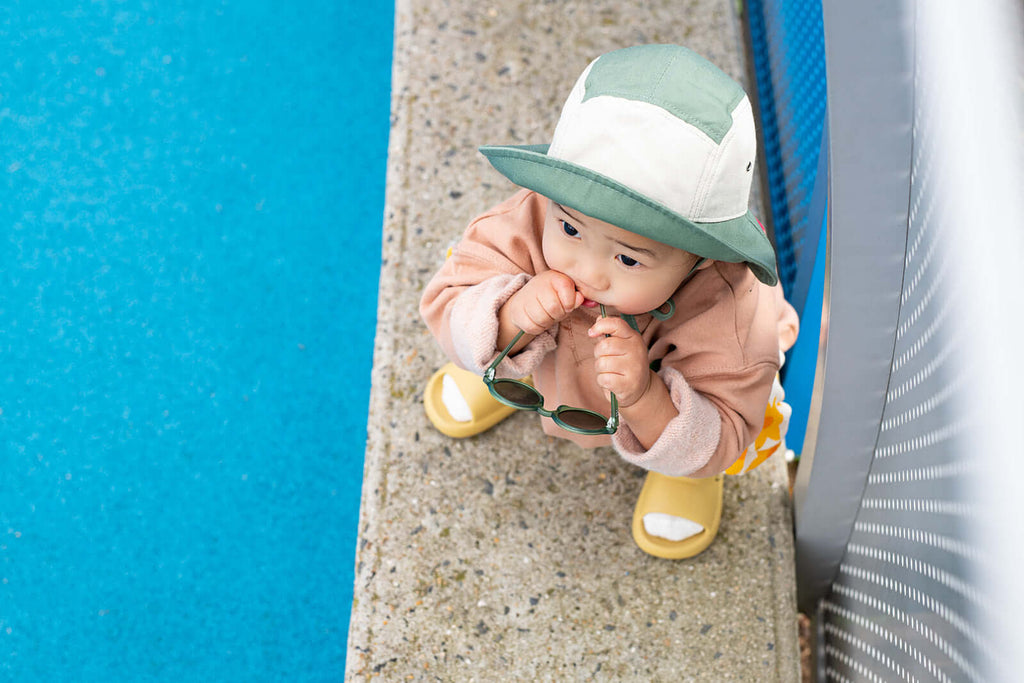 Baby biting sunglasses with hat on